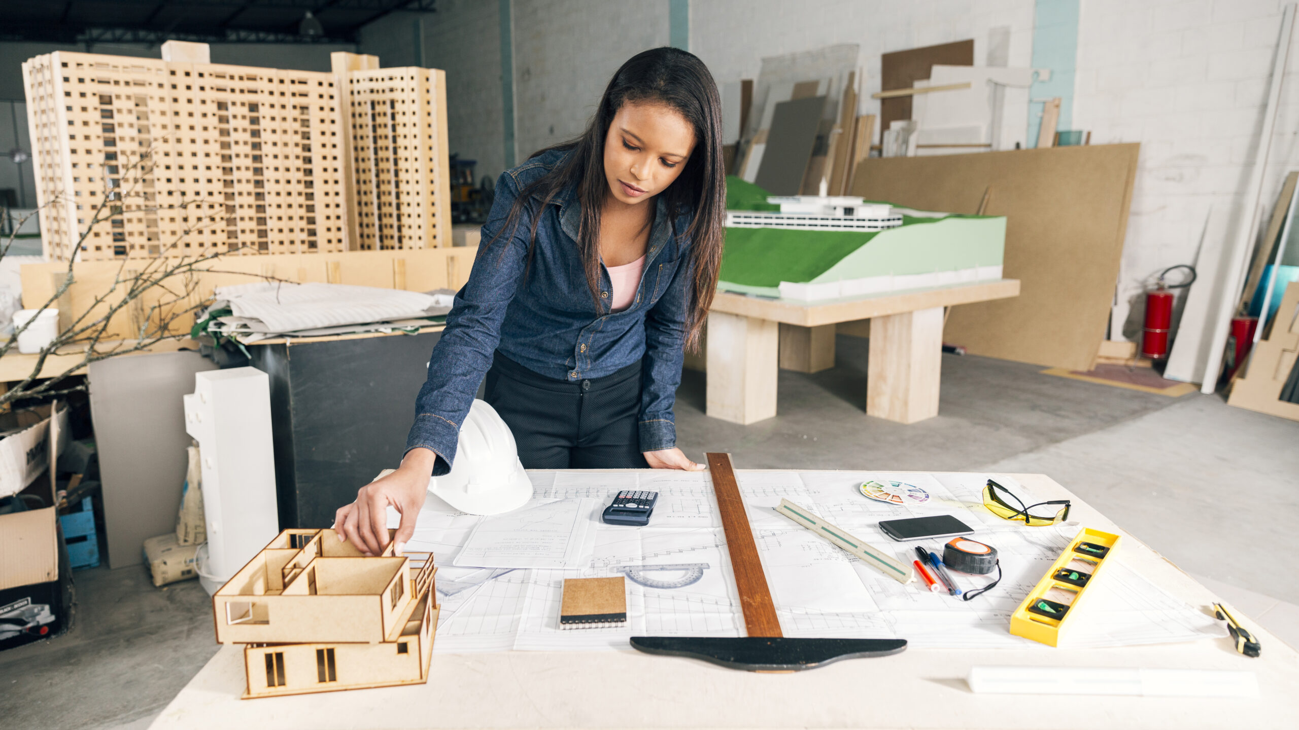 arquiteta com uma casa modelo na mesa, perto de um capacete de segurança e equipamentos.